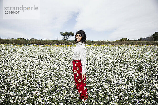 Smiling young beautiful woman standing amidst white flowers at field