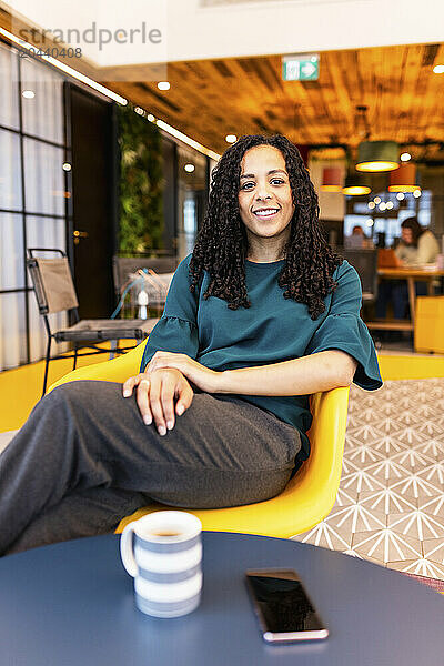 Smiling businesswoman sitting on chair at coworking office