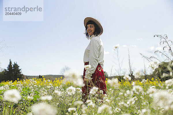 Smiling young woman standing amidst flowers at meadow