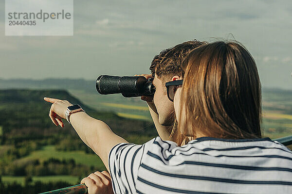 Young couple looking through binoculars from observation point