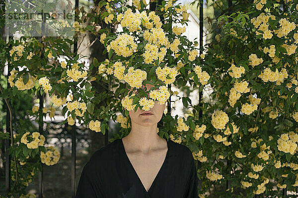 Woman hiding face behind yellow flowers at park