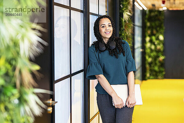 Smiling businesswoman with laptop standing near wall at coworking space