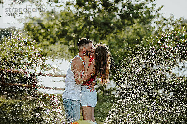 Affectionate couple kissing near ball splashing water at garden