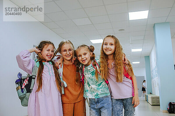 Cheerful schoolgirls standing with arm around in school corridor