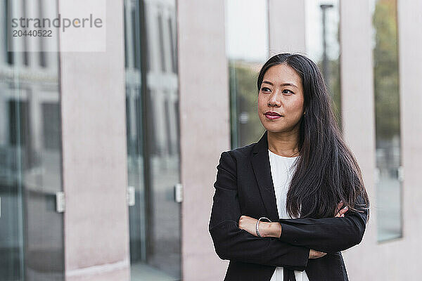 Thoughtful businesswoman standing with arms crossed at office park