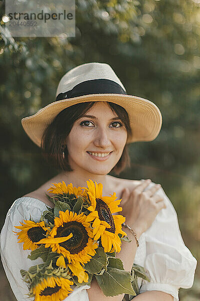 Young woman wearing hat and holding sunflowers at field