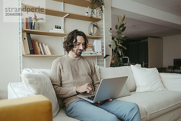 Businessman using laptop sitting on sofa in living room