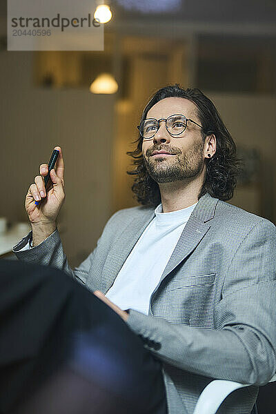 Thoughtful businessman sitting with pen in office