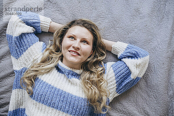 Smiling woman lying on bed with hands behind head