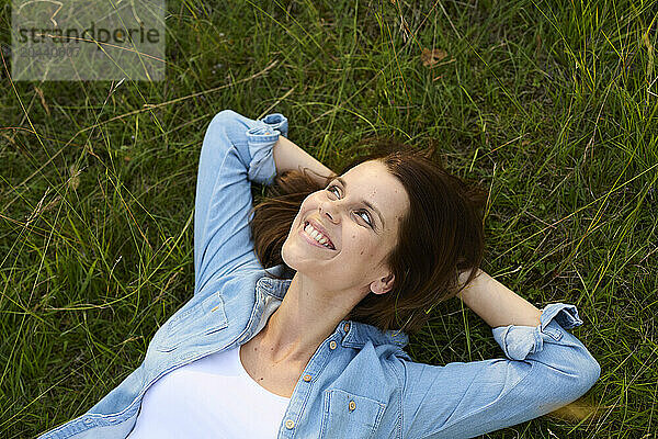 Happy woman with hands behind head lying on grass