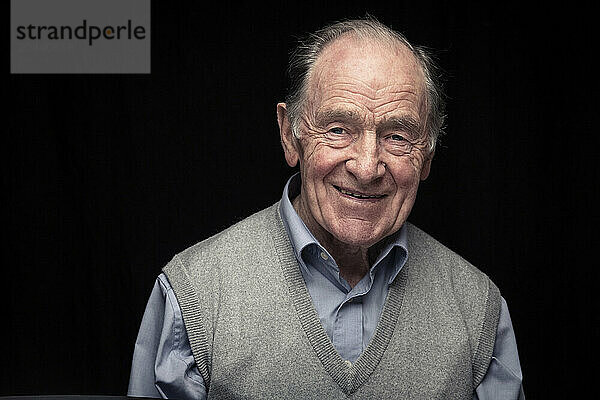 Senior man wearing sweater standing against black background