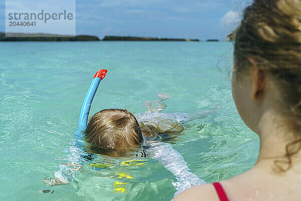 Girl snorkeling near mother in sea on sunny day