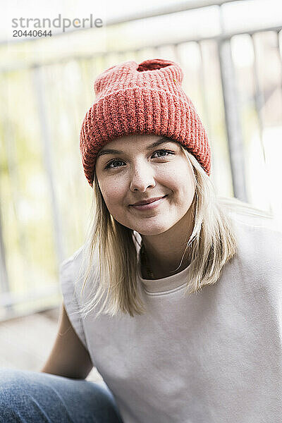 Smiling woman wearing knit hat sitting on balcony