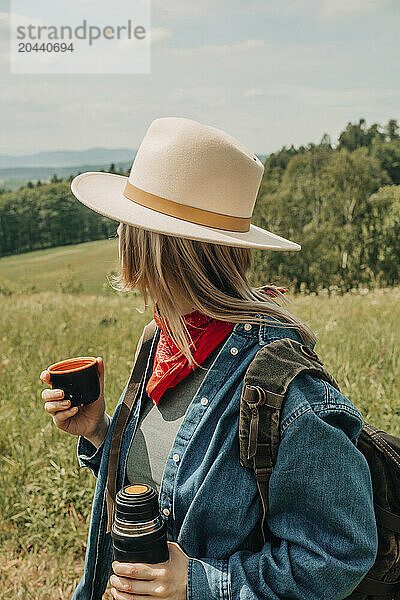 Woman wearing hat and backpack drinking warm tea in mountains