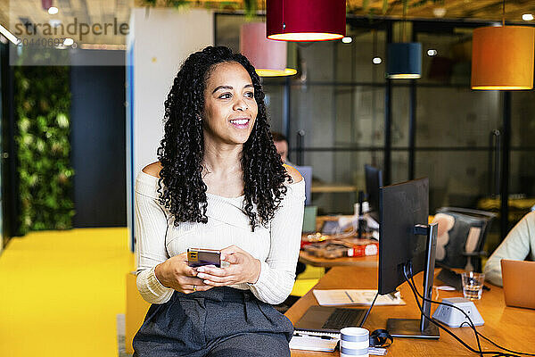 Smiling businesswoman holding smart phone at coworking space