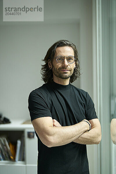 Confident businessman standing with arms crossed at office