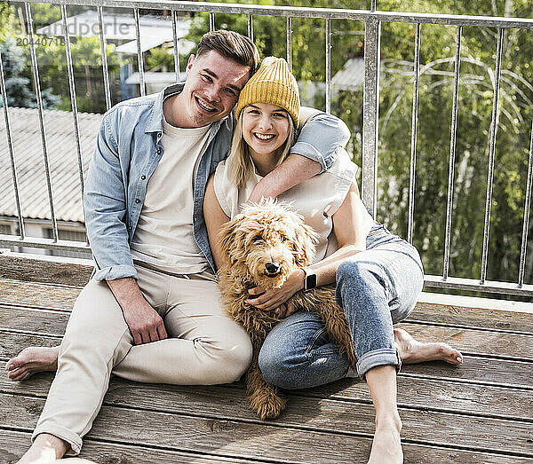 Happy man and woman sitting with dog on balcony