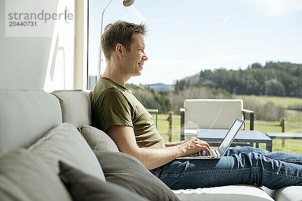 Mature man working on laptop by window at home