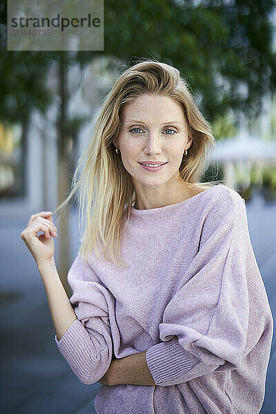 Beautiful blond hair woman wearing purple sweater and standing at street