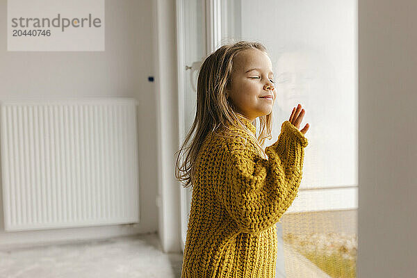 Girl leaning on window with eyes closed in new apartment