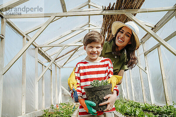 Happy boy and mother carrying potted plant at greenhouse