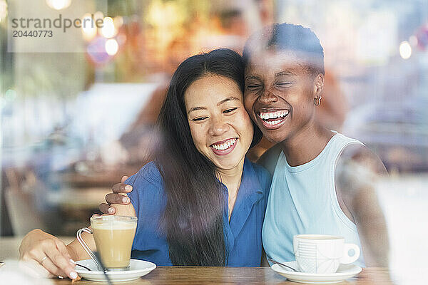 Happy multiracial friends drinking coffee sitting at table in cafe