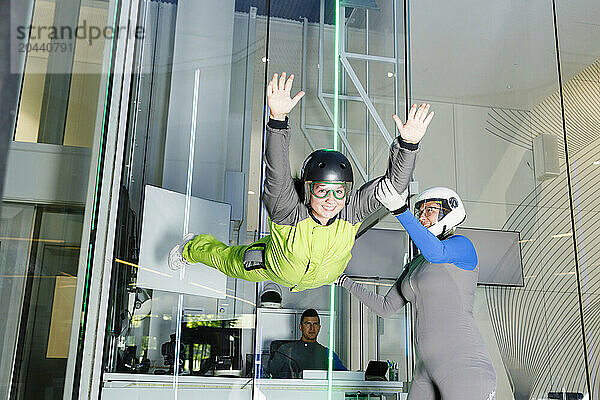 Happy instructor giving free falling training to girl at indoor skydiving center