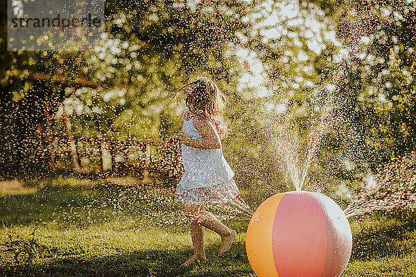 Girl dancing by colorful ball splashing water at garden