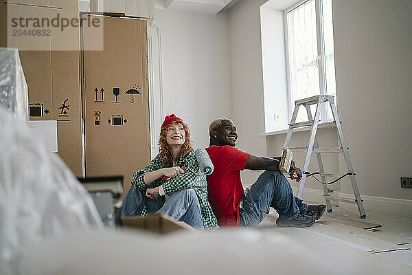 Happy friends sitting with paint roller and brush near boxes at home