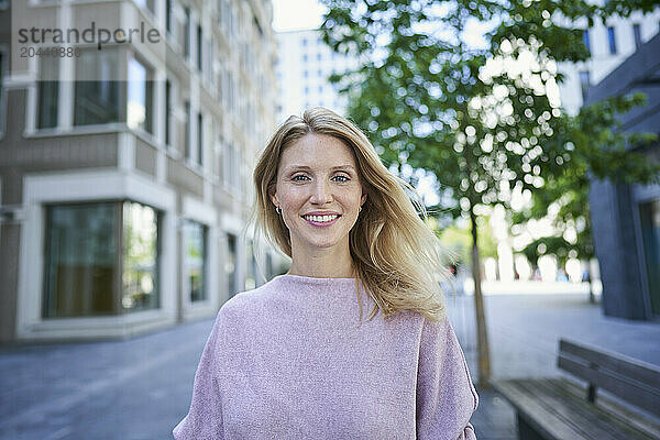 Beautiful blond hair woman wearing purple sweater standing near building