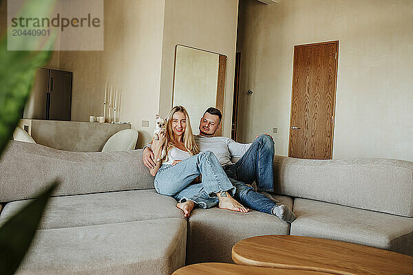 Happy couple sitting on sofa with dog at home