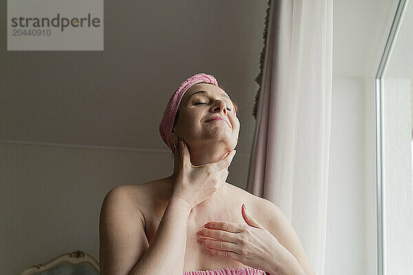 Woman with head towel massaging face at home