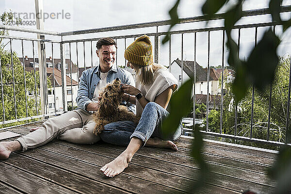 Happy man and woman playing with dog on balcony