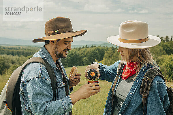 Couple wearing hats enjoying warm tea in meadow