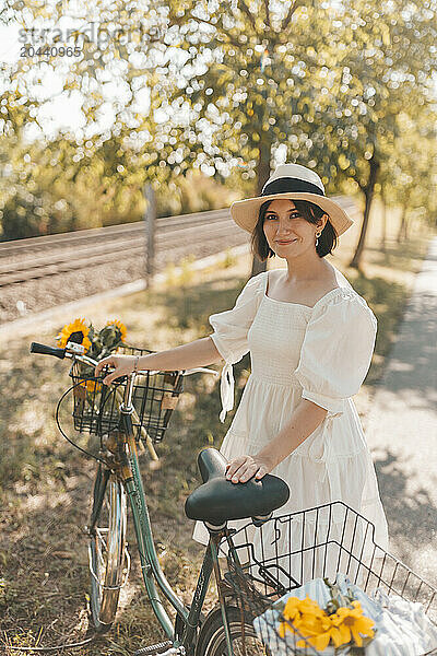 Smiling young woman wearing hat and standing near bicycle