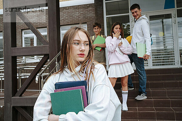 Students bullying teenage girl with books at schoolyard