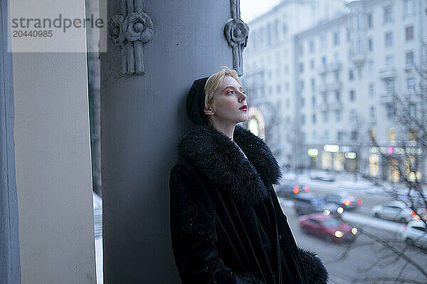 Young woman wearing winter coat and leaning on column in balcony