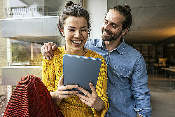 Happy young couple using tablet PC together by window at home