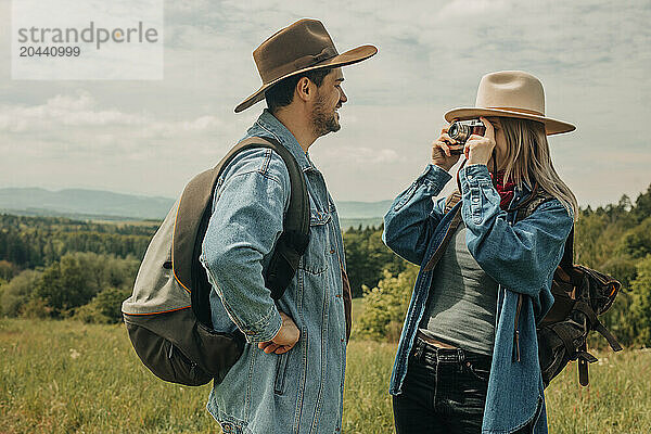 Woman picturing man with hand on hip wearing hat on sunny day