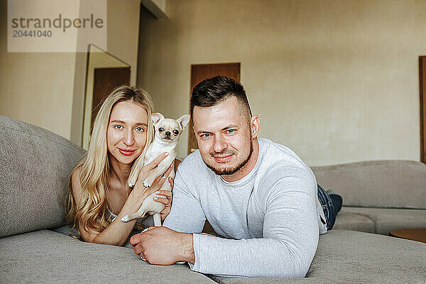 Smiling couple lying on sofa with dog at home