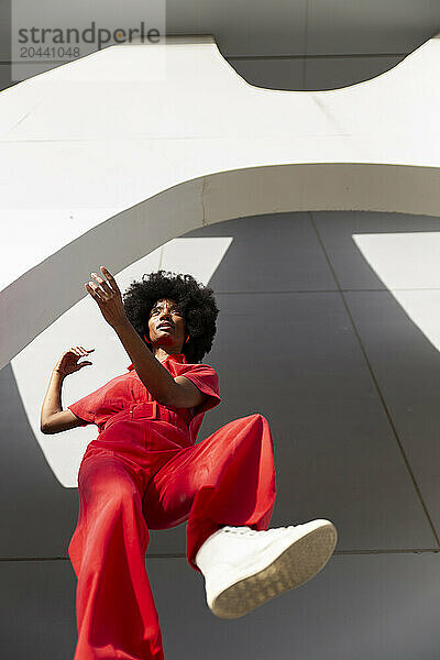 Mature woman wearing red jumpsuit and standing under modern building