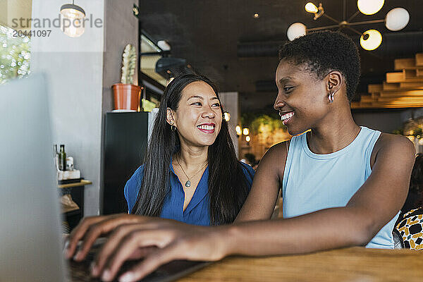 Happy friends sitting with laptop sitting in cafe