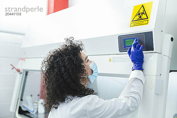 Scientist with mask operating fume hood in laboratory