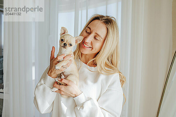 Smiling young woman holding chihuahua dog at home