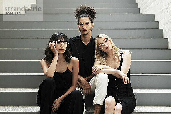 Male and female friends wearing eyeglasses sitting on steps