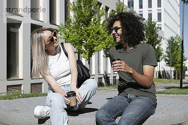 Happy man and woman wearing sunglasses talking in park on sunny day