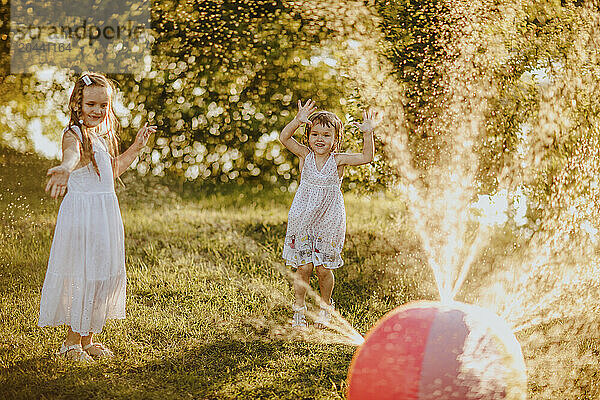 Sisters dancing by colorful ball splashing water at garden