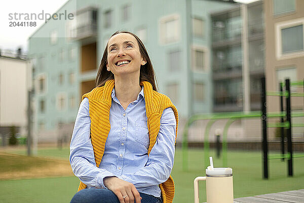 Happy beautiful woman wearing sweater on neck and sitting at park