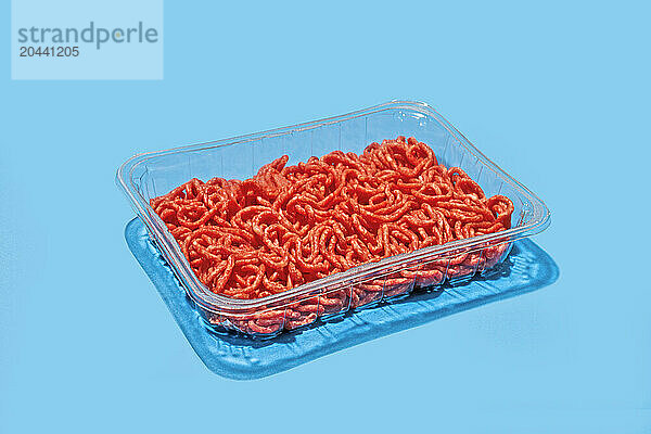 Plastic tray with ground beef from supermarket on blue background