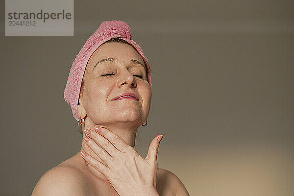 Woman with head towel massaging neck at home